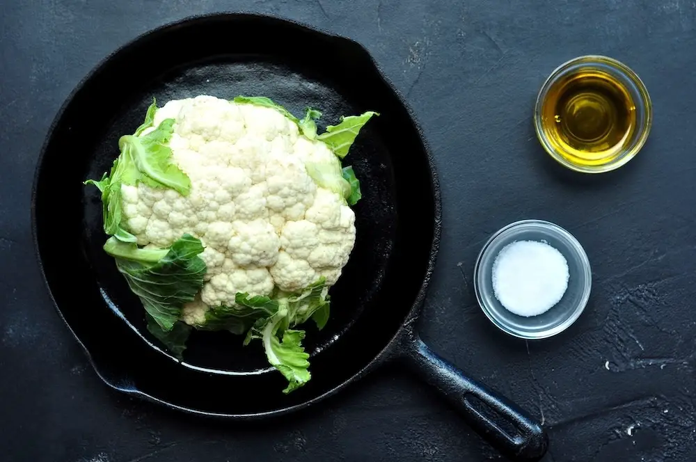 A whole head of cauliflower in a skillet ready to be seasoned with olive oil and salt