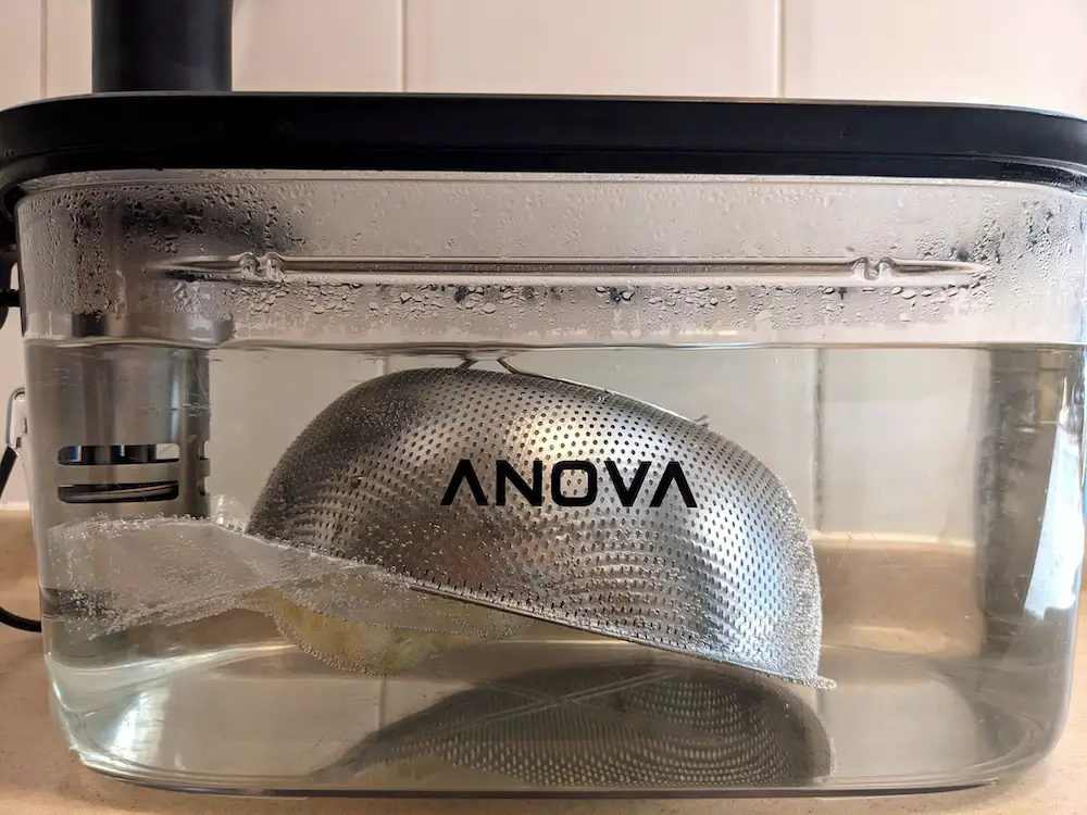 Whole cauliflower weighed down in the sous vide bath by an inverted colander.