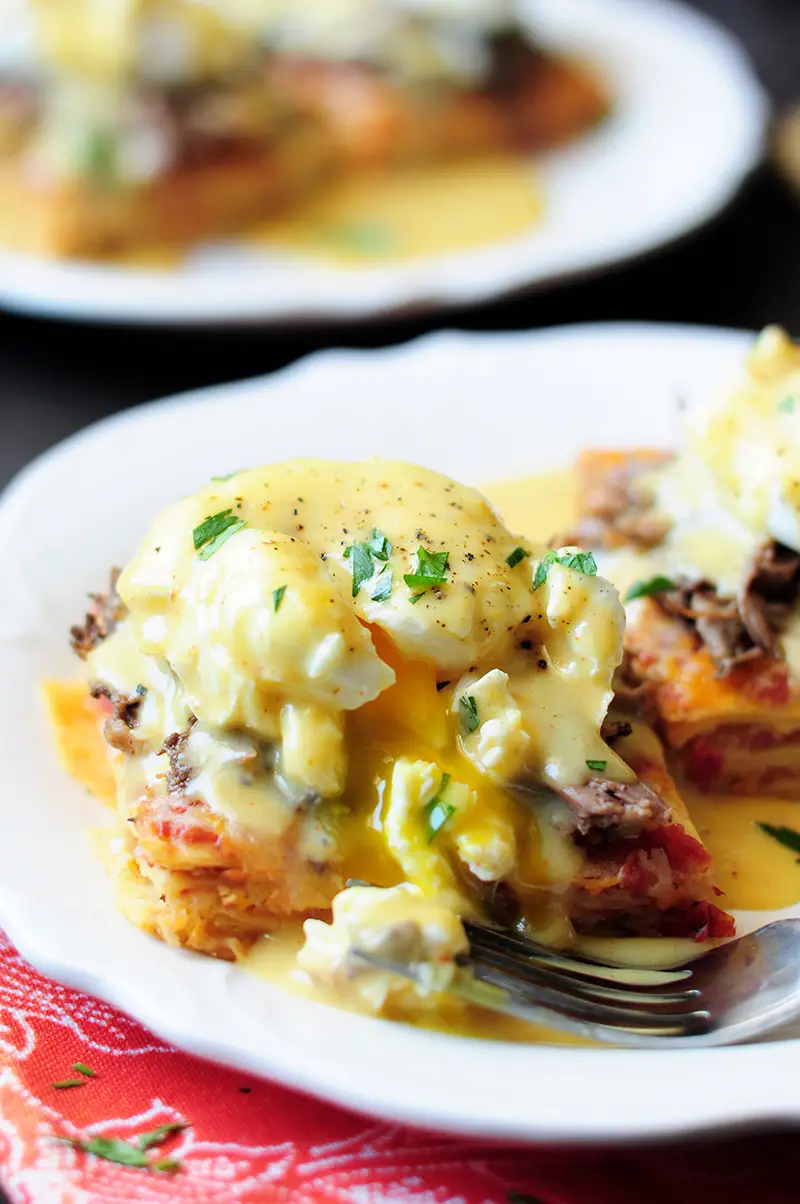 This is a unique Eggs Benedict recipe with slow cooked barbacoa and a green chili hollandaise served on a chilaquiles base.