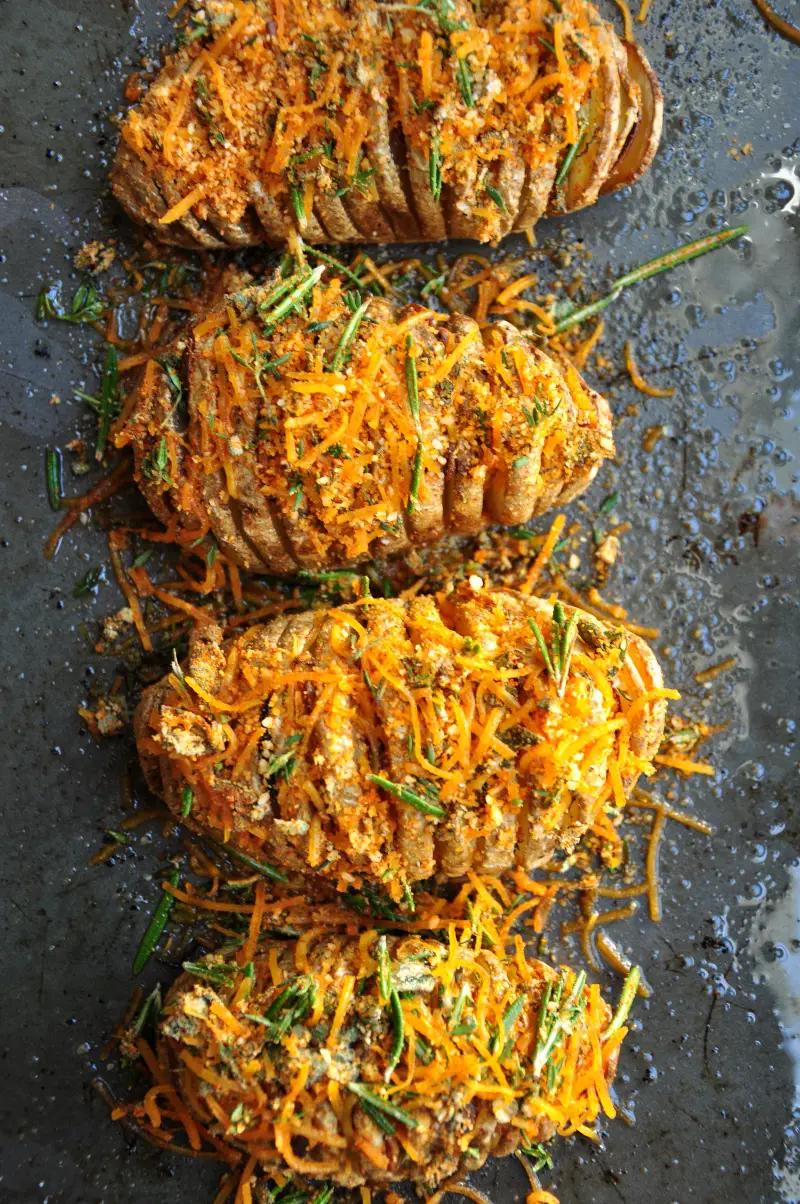 Perfectly baked hasselback potatoes with garlic slices in between, brushed with infused butter, topped with cheddar, parmesan, and three freshly chopped herbs.