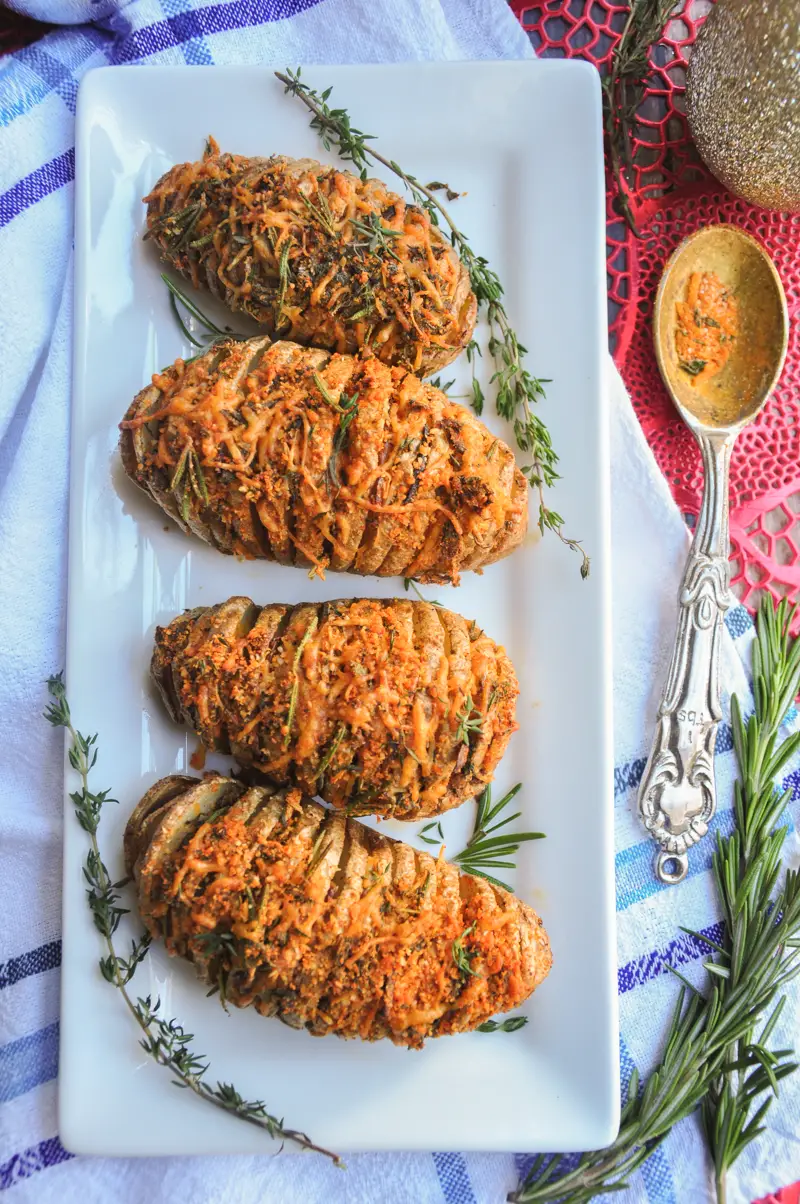 Perfectly baked hasselback potatoes with garlic slices in between, brushed with infused butter, topped with cheddar, parmesan, and three freshly chopped herbs.