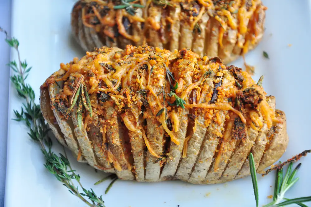 Perfectly baked hasselback potatoes with garlic slices in between, brushed with infused butter, topped with cheddar, parmesan, and three freshly chopped herbs.