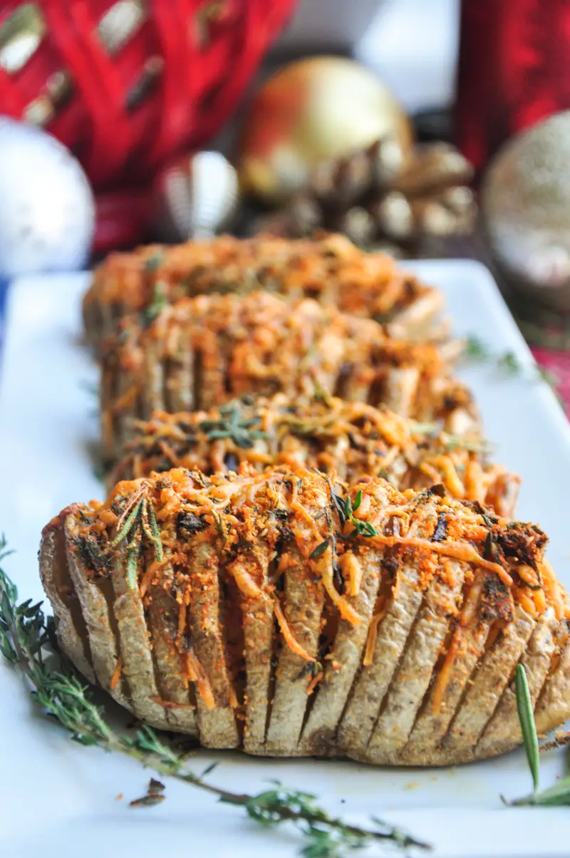 Perfectly baked hasselback potatoes with garlic slices in between, brushed with infused butter, topped with cheddar, parmesan, and three freshly chopped herbs.