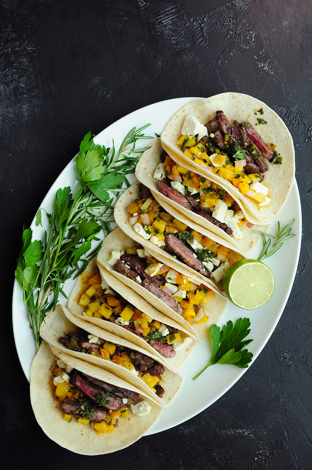 Skirt steak tacos lined up on a large oval plate