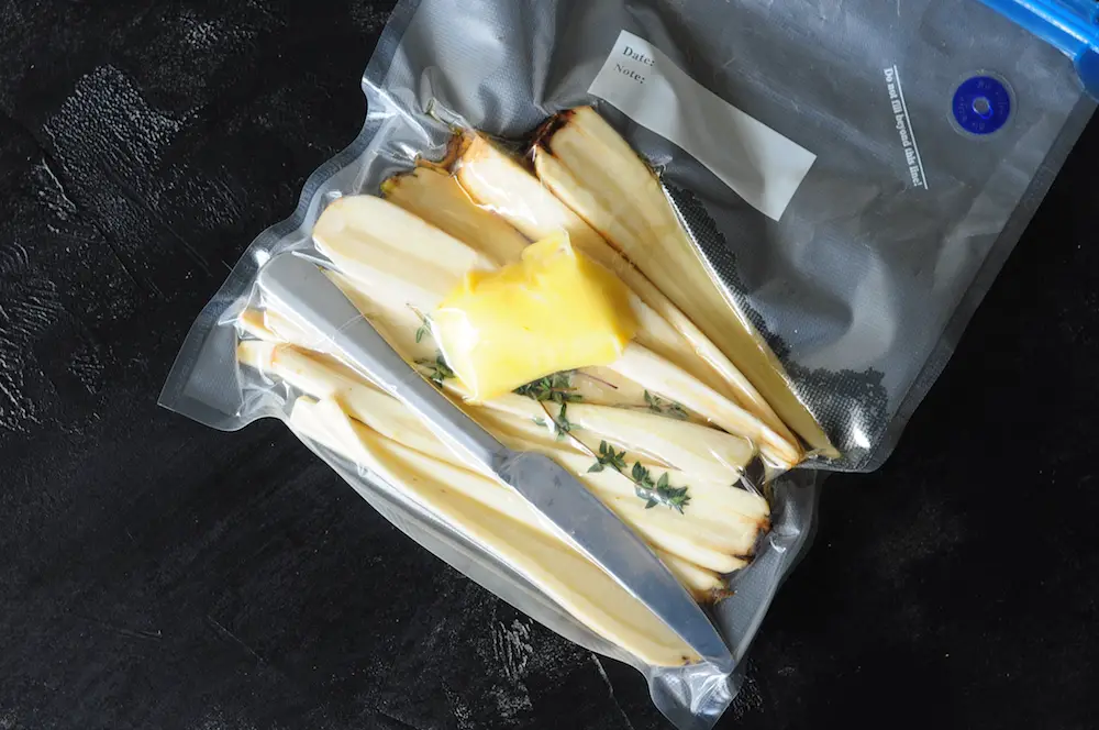 A butter knife inside a vacuum sealed sous vide bag with carrots, butter, and thyme